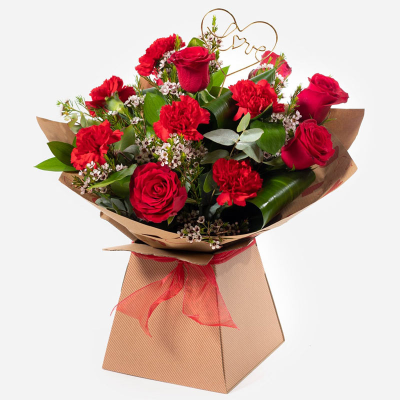 Love in Bloom - A romantic arrangement of rich red roses and carnations, finished with delicate blooms and lush greenery in a stylish kraft box.